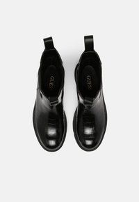 Black ankle boots in glossy crocodile-embossed material, featuring elastic side panels and pull tabs for easy wear. Flat, textured sole.