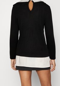 Svart långärmad topp med vit krage och en nyckelhålöppning på baksidan, tillverkad av mjukt tyg med en figurnära design.