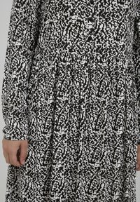 Mekko mustavalkoisella kuvioinnilla, jossa on pitkät hihat, nappikiinnitys edessä ja rypytetty vyötärö, valmistettu kevyestä kankaasta.