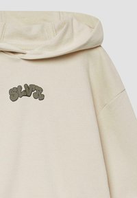 Beige hoodie met een groot, gestileerd "SLVR" logo in donkergroen op de borst. Voorzien van een capuchon met trekkoord en een zachte textuur.