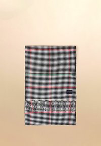 Složená černobílá šála se vzorem psího zubu, s červenými a zelenými kostkovanými pruhy, třásněmi na okrajích a malou obdélníkovou značkovou štítkem.