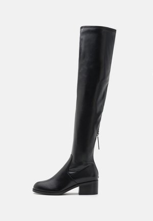 Botte haute en cuir noir avec un petit talon bloc et une fermeture éclair sur le côté, présentée en profil sur un fond blanc uni.