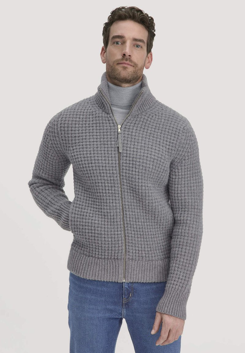 Grau gestrickter Zip-Up-Pullover mit hohem Kragen, strukturiertem Muster, geripptem Saum und Bündchen, kombiniert mit einem grauen Rollkragenpullover und blauen Jeans.