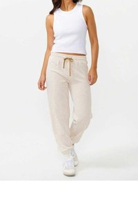 Beiga joggers med elastisk midja och justerbar dragsko. Kombineras med en åtsittande vit tanktopp och vita sneakers. Slät yta.