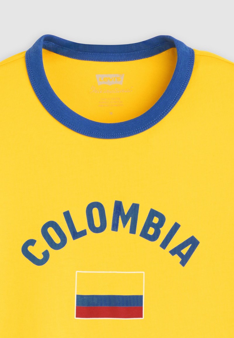 T-shirt jaune avec col bleu, "COLOMBIA" en lettres bleues et un drapeau rectangulaire avec des bandes horizontales jaunes, bleues et rouges.