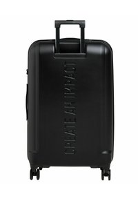 Valigia rigida nera con una superficie testurizzata. Presenta un manico retrattile, due ruote e del testo in rilievo "CREA UN IMPATTO."