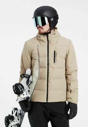 Chaqueta de plumas beige, con cierre frontal y detalles en negro. Casco negro con visor reflectante. La tabla de snowboard y los fijaciones son blancas con detalles en negro.