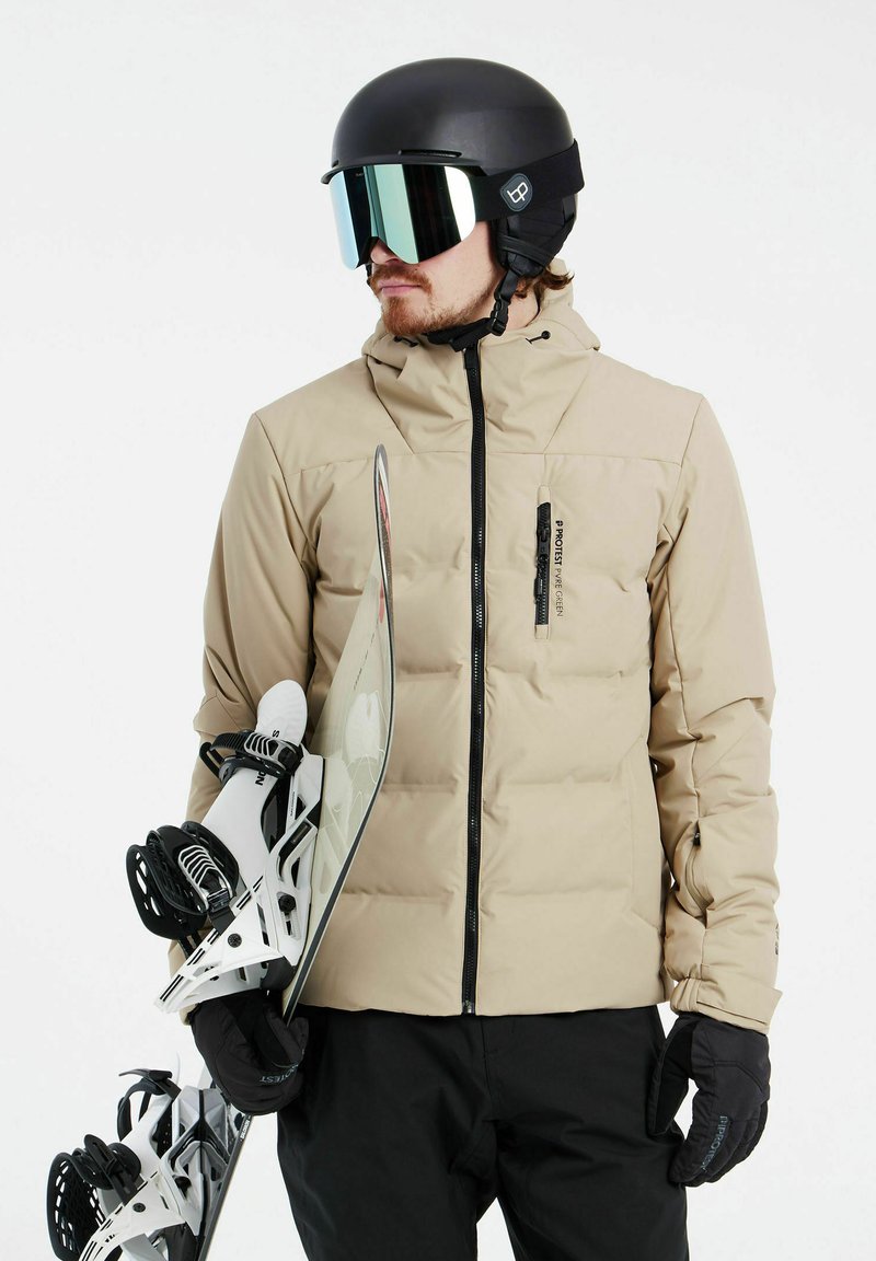Beige Steppjacke mit Reißverschluss, schwarze Akzente. Schwarzer Helm mit verspiegeltem Visier. Snowboard und Bindungen sind weiß mit schwarzen Details.