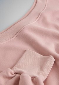 Close-up van zacht roze sweatshirtstof met geribbelde manchetten en naaddetails op een gladde achtergrond.