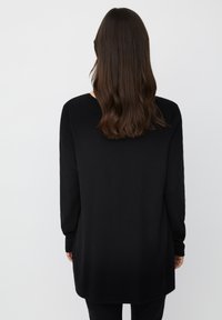Tunic nera a maniche lunghe con scollatura rotonda, texture liscia, vestibilità rilassata e orlo posteriore leggermente allungato.