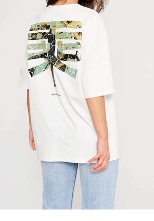 Camiseta blanca de gran tamaño con un diseño gráfico texturizado en verde, dorado y negro en la parte posterior. Material de algodón, mangas cortas.