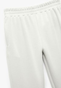 Lys grå sweatpants lavet af blødt stof, med elastisk talje og sidelommer, og en glat, let struktureret overflade.