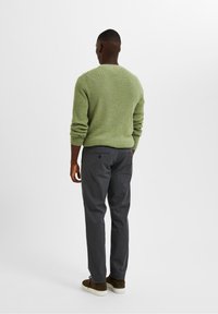 Groen gestructureerd gebreid trui, donkergrijze broek en bruine suède schoenen. Uitzicht van achteren, dat de pasvorm en kleurcombinatie van de outfit toont.