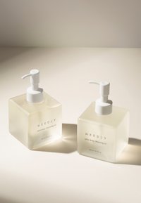 Dwie kwadratowe butelki z matowego szkła z białymi pompkami, oznaczone jako "NEEDLY Mild deep cleansing oil", każda zawierająca 240 ml.