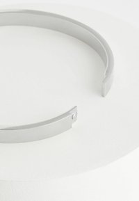 Sølvmetal cuff armbånd med mat finish, åben design, der har en lille gemstone accent og en geometrisk form.