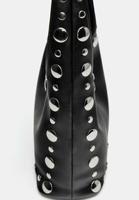 Czarna skórzana torba z dużymi srebrnymi ćwiekami ułożonymi w wzór po bokach, o miękkiej fakturze i wyraźnej strukturze.