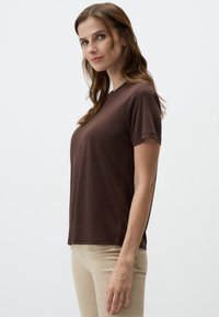 Bruine T-shirt met korte mouwen, gemaakt van zachte stof, met een ronde halslijn en een ontspannen pasvorm, gecombineerd met lichtbeige broek.