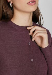 Cárdigan de punto ligero en color ciruela oscuro, con cuello redondo, botones frontales y puños acanalados. Textura suave, brillo sutil y diseño ajustado.