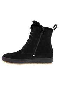 Botas negras de ante hasta el tobillo con un cuello de peluche, lazo frontal y cremallera lateral. Tienen suela de tracción de goma y un logo mínimo.