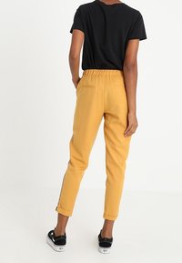 Gula byxor med elastisk midja och uppvikta ben, med sidostråk. Matchas med en svart t-shirt med kort ärm och svarta sneakers.