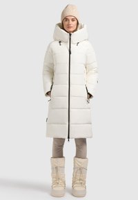 White puffer coat with large hood, zip closure, and front pockets, paired with beige snow boots featuring laces and a textured finish.