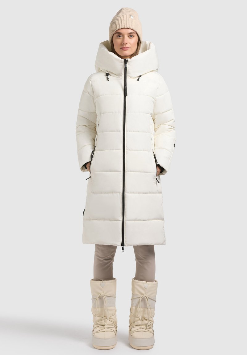 White puffer coat with large hood, zip closure, and front pockets, paired with beige snow boots featuring laces and a textured finish.