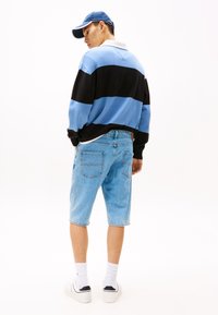 Stripet genser i blått og svart, denimshorts, hvite sokker og joggesko. Genseren har krage og avslappet passform, shortsene er knelange.