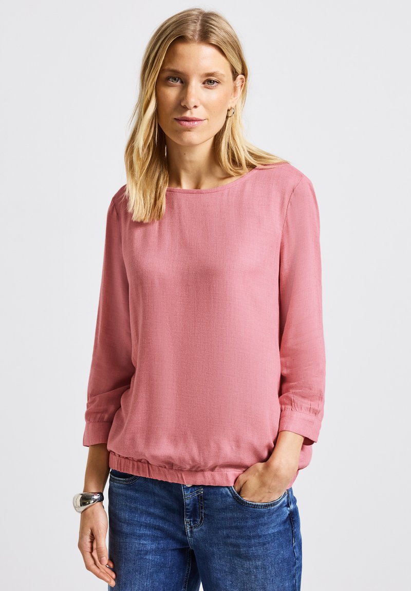 Blusa rosa con finitura testurizzata, maniche a tre quarti e vestibilità morbida. Collo rotondo e orlo inferiore elasticizzato.