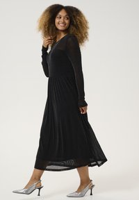 Black, long-sleeve dress with a fitted bodice and flared skirt. Made of textured, sparkly fabric. Paired with silver, pointed-toe heels.