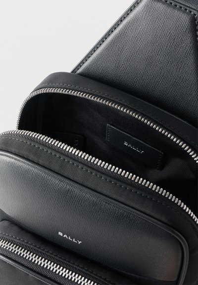 Sac Bally en cuir noir texturé avec deux compartiments ouverts et fermetures éclair argentées, arborant le logo Bally à l'avant et sur la doublure intérieure.