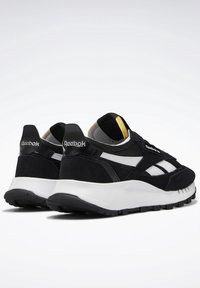 Baskets Reebok noires et blanches avec semelles blanches épaisses, dessus en mesh noir et en daim, logo visible au talon et sur le côté, vue en angle par l'arrière.