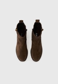 Botas de tobillo de ante marrón con una textura suave, punta redondeada, cremallera lateral y un tacón bajo. Presenta una tira en la parte posterior para facilitar su colocación.