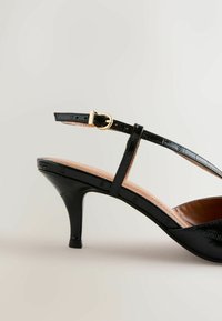 Sort laklædersko med høje hæle, spids tå, anklerem og guldfarvet spænde. Glat tekstur med et subtilt krokodillemønster.