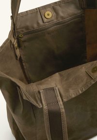 Brown canvas tote bag with a zippered interior pocket, brass snap closure, and sturdy fabric straps. Features a smooth, textured finish.