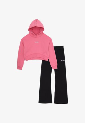 Felpa rosa corta con tasca a marsupio frontale e pantaloni neri a zampa d'elefante, entrambi con logo "PYREX" in bianco, in materiale cotone.