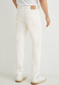 Vaqueros de denim de color claro con un corte ajustado, diseño de cinco bolsillos y una etiqueta de cuero en la cinturilla. Presenta costuras blancas y un detalle mínimo.