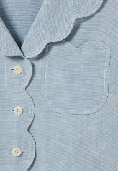 Camicia azzurro chiaro con colletto ondulato, cuciture bianche e quattro bottoni, dotata di una tasca decorativa a forma ondulata.
