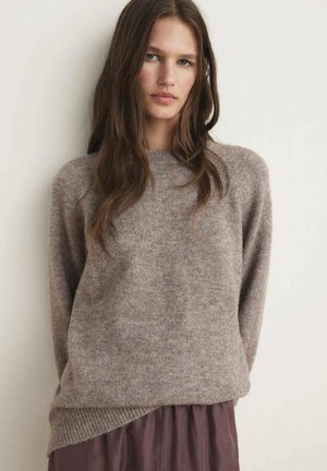 Light brown knitted sweater with a ribbed neckline and long sleeves, layered over a darker brown skirt, creating a contrast in textures.