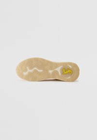 Semelle de sneaker en caoutchouc beige clair avec un motif texturé et ondulé et une marque discrète en jaune, dotée d'un bord extérieur épais et courbé.