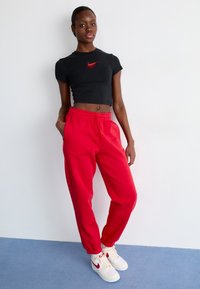 Čierny crop top s červeným logom Nike, v kombinácii s červenými teplákmi so stiahnutými manžetami a bielymi teniskami Nike s červenými akcentmi.