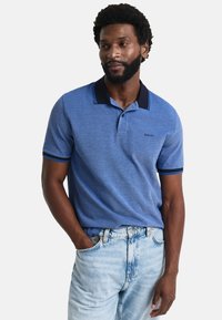 Modrá polokošile s námořnickým límečkem a pruhovanými detaily, vyrobená z měkkého materiálu. Nosená s světle modrými džíny. Obsahuje logo.