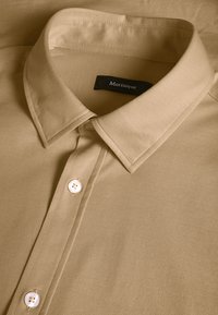 Khaki košela na gombíky s tradičným golierom, štruktúrovanou textúrou látky a bielymi gombíkmi. Štítok označuje "Matinique."