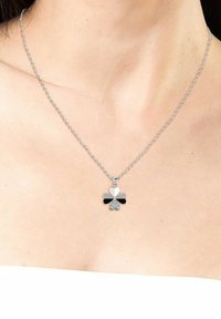 Zilveren ketting met een klavertje vier hanger, gekenmerkt door contrasterende zwarte en witte secties, verfraaid met een kleine steen aan de onderkant.