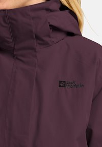 Lila wasserfeste Jacke mit hohem Kragen und verstellbarem Kapuze; verfügt über ein gesticktes Logo in Schwarz. Weicher, texturierter Stoff.