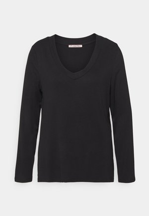 Chemise noire à manches longues avec col en V en tissu doux, présentée à plat avec une étiquette visible au niveau du cou indiquant "Anna Field."