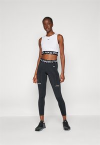 Nike Pro sportski grudnjak u bijeloj boji s crnim logotipom; crne tajice s bijelim logotipom; lagani, rastezljivi materijal; uski dizajn; atletske cipele.
