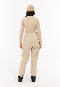 Beige top met lange mouwen en losse beige broek met elastische taille, zijzak en knoopmanchetten, gecombineerd met een gebreide beige muts.