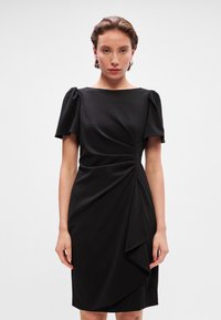 Melnas kleitas ar īsām pūkām, apaļu dekoltē, drapēta auduma ar viļņotu detaļu un pieguļošu siluetu. Gluda tekstūra.