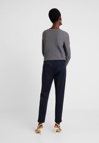 Szary dzianinowy sweter o luźnym kroju, w połączeniu z granatowymi spodniami z bocznymi kieszeniami i podwiniętymi mankietami. Model ma na sobie beżowe sandały na obcasie.