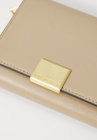 Portafoglio in pelle beige con finiture dorate e logo impresso, con bordi cuciti e una consistenza liscia. Forma rettangolare.